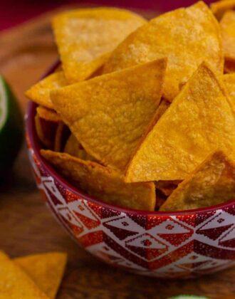 A bowl of air fryer tortilla chips on a wooden cutting board with sliced limes on the side