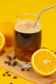 An iced coconut water americano on a yellow table next to a sliced orange