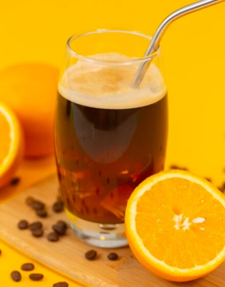 An iced coconut water americano on a yellow table next to a sliced orange