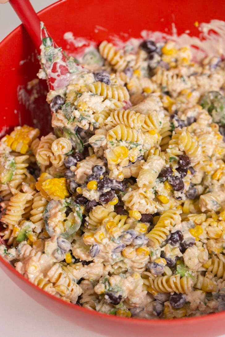 Alyssia using a large silicon spatula to finally mix all the ingredients of her Easy Mexican Street Corn Pasta Salad together.