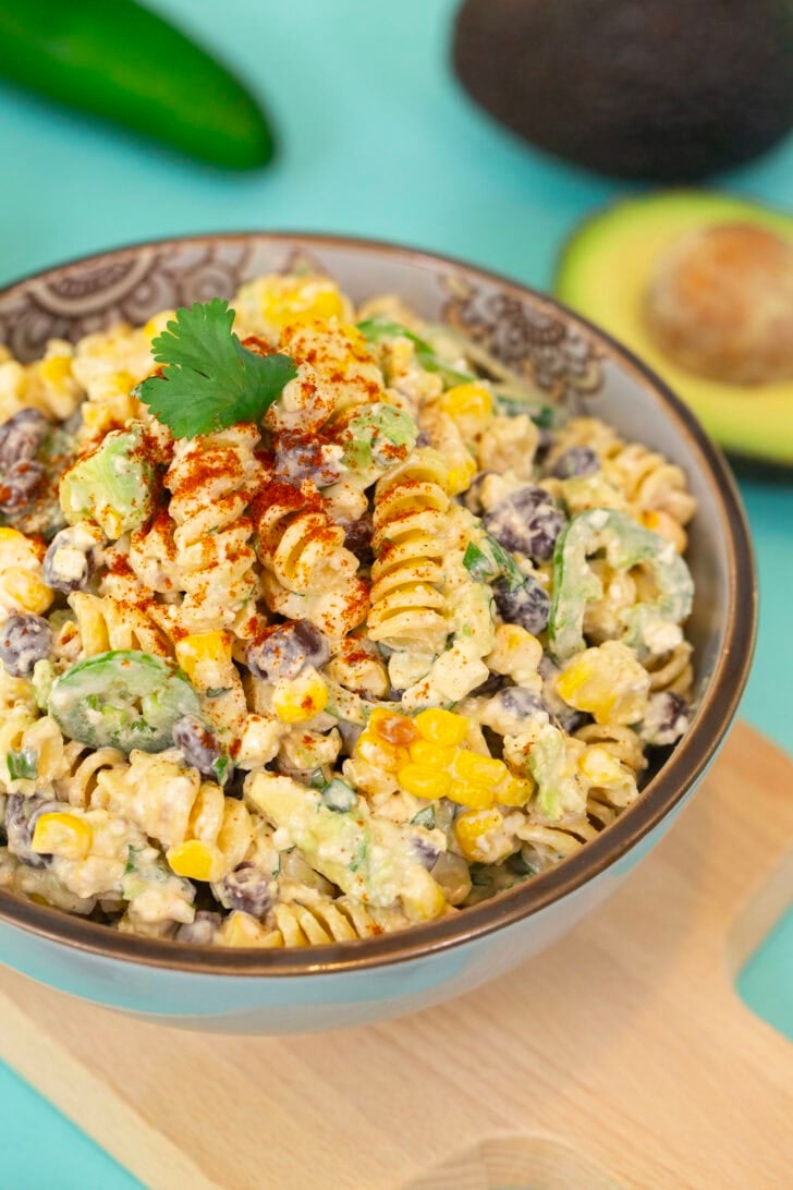 A portrait shot of the Mexican Street Corn Pasta Salad, on a blue table surrounded with ingredients.