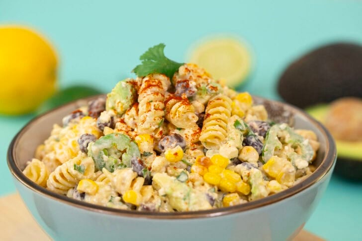Another side profile shot of the Mexican Street Corn Pasta Salad, again on a blue table surrounded with ingredients.