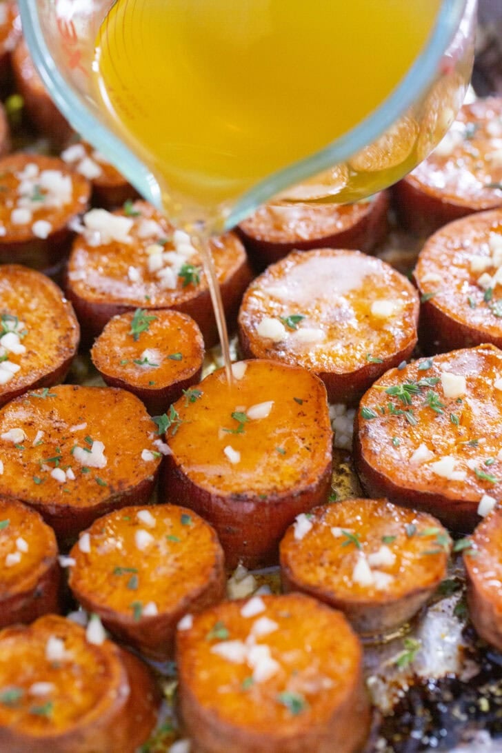 Pouring broth over the caramelized rounds of maple brown butter melting sweet potatoes with glaze and herbs