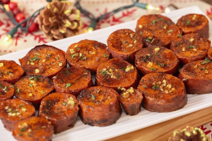 A plate with caramelized rounds of maple brown butter melting sweet potatoes with glaze and herbs