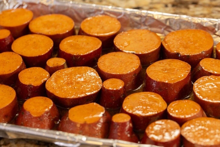Sliced rounds of sweet potato in a baking dish lined with foil, covered in brown butter glaze.
