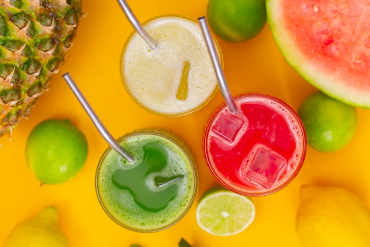 An overhead photo of three glasses of agua fresca, cucumber, pineapple, and watermelon flavors.
