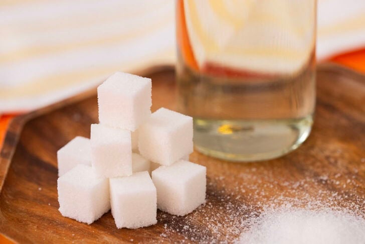 A close up photo of a pile of sugar cubes with a bottle of simple syrup in the background.