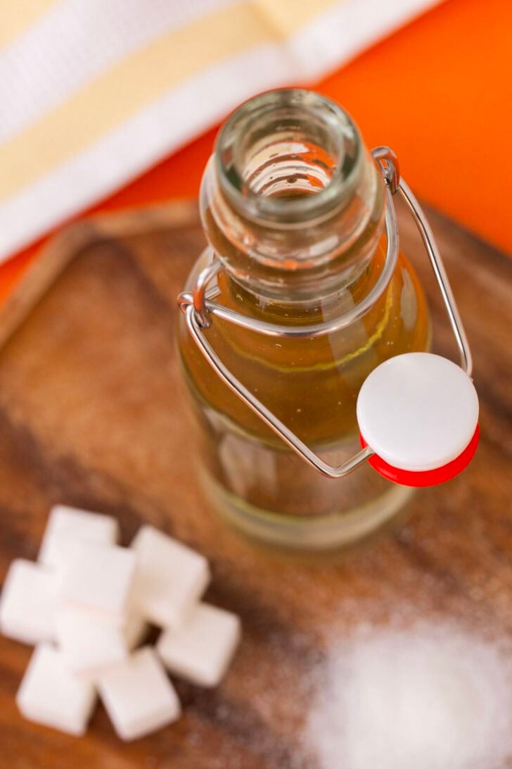 An open bottle of simple syrup, with a pile of sugar cubes in the background.