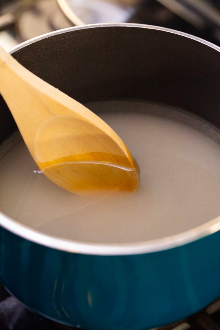 Using a wooden spoon to stir sugar and water in a pot over the stove.
