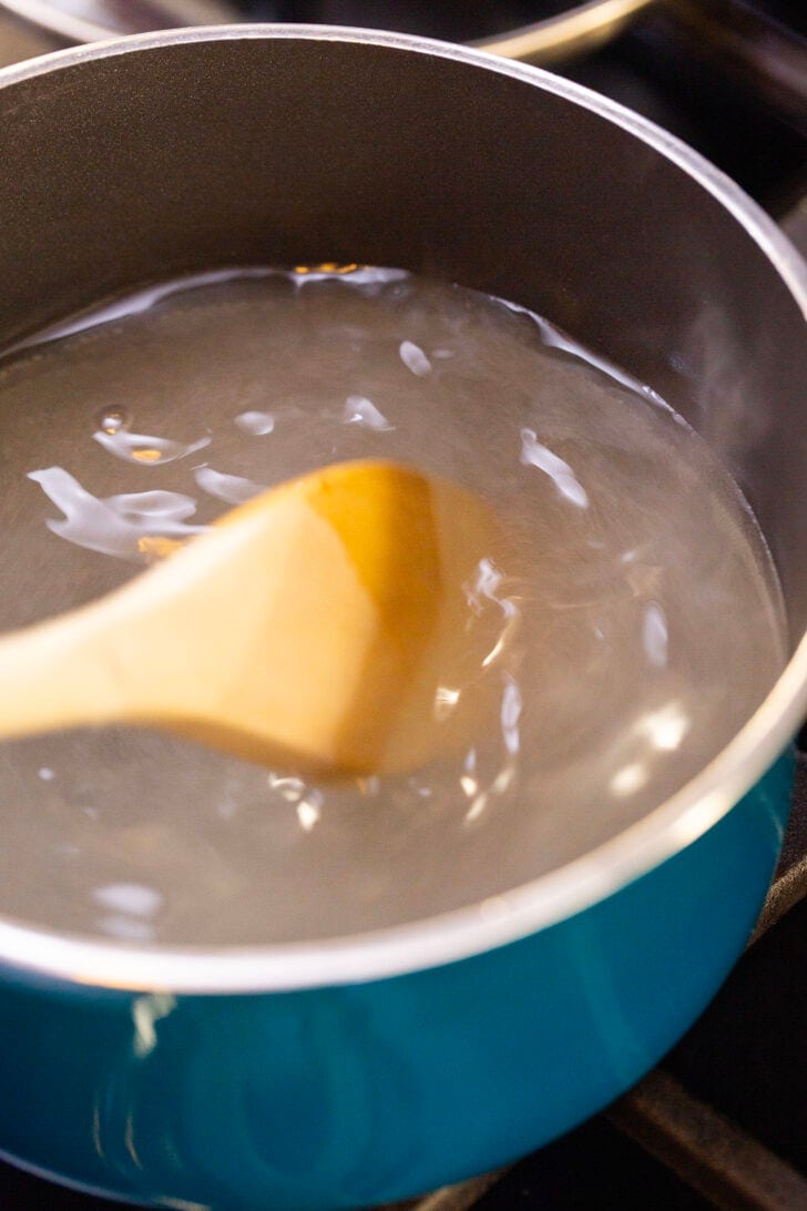 Stirring the sugar and water mixture with a wooden spoon and watching the sugar dissolve.