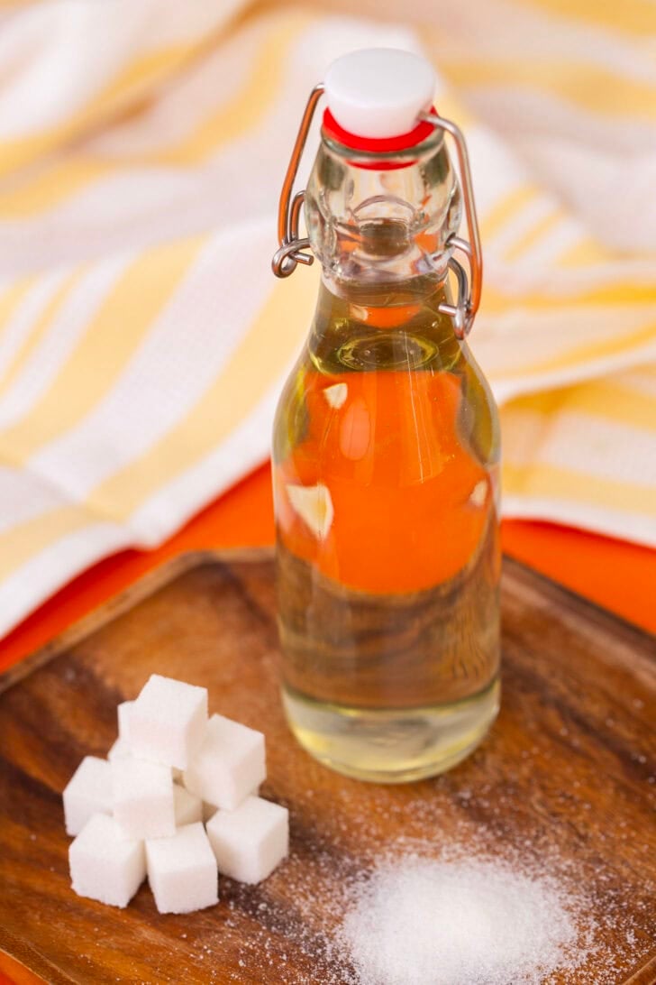 The same bottle of simple syrup next to a pile of sugar cubes on a wooden cutting board.