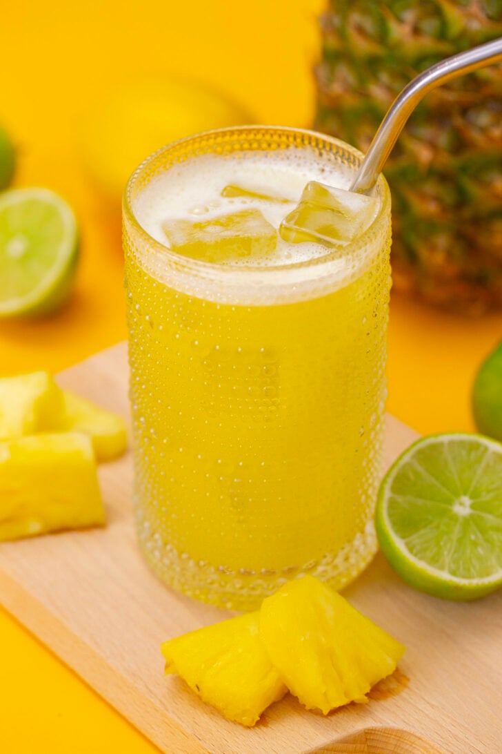Pineapple agua fresca in a glass, sitting on a cutting board surrounded by ingredients.