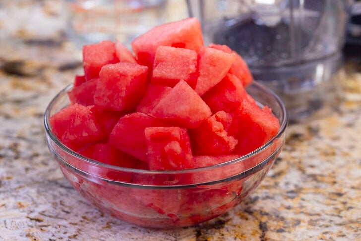 Cubed watermelon in a glass bowl on a counter.