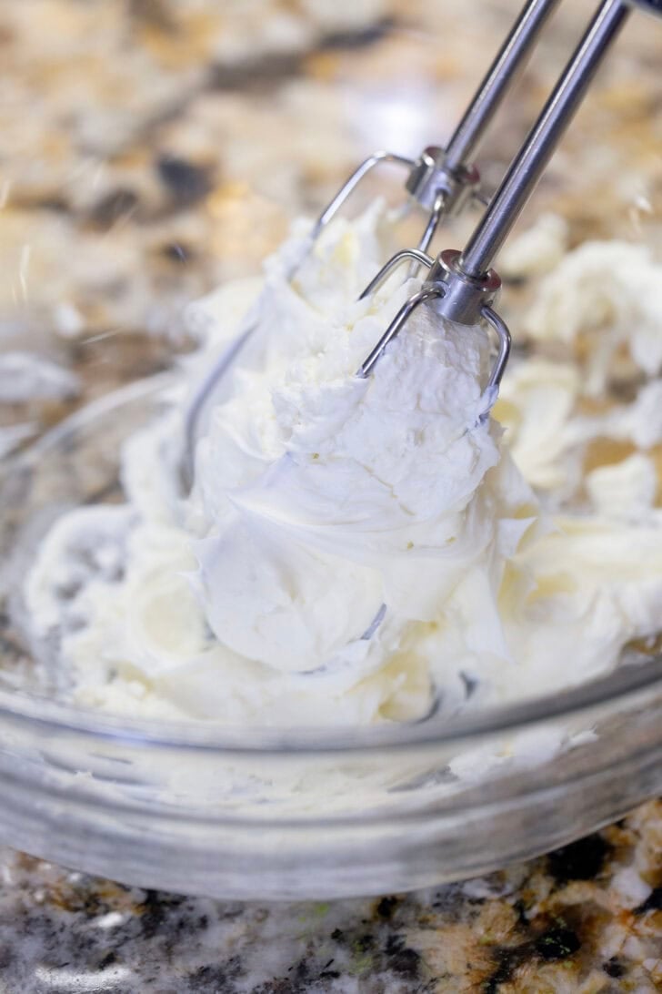 Whipping cream cheese in a bowl using a hand mixer.