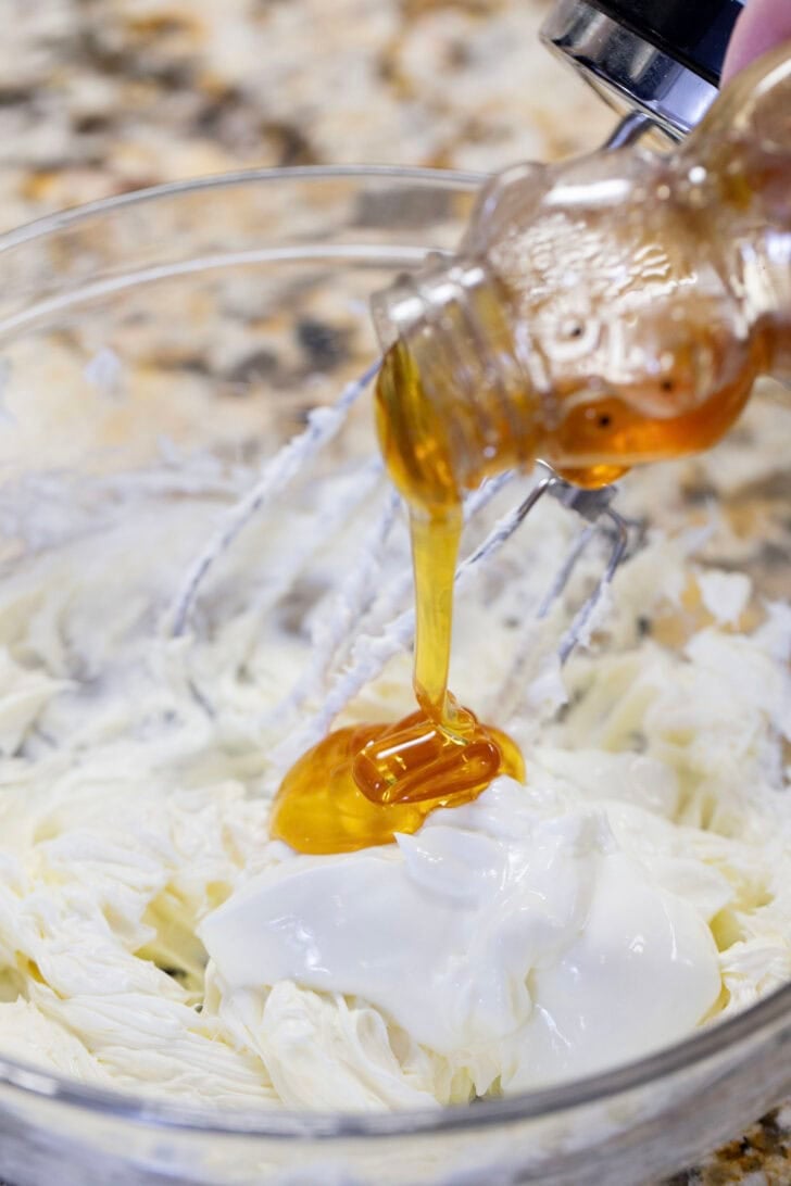 Adding honey and greek yogurt into a bowl of whipped cream cheese.