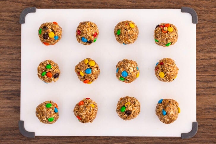 A white cutting board with twelve rolled protein balls, organized in a 3x4 grid.