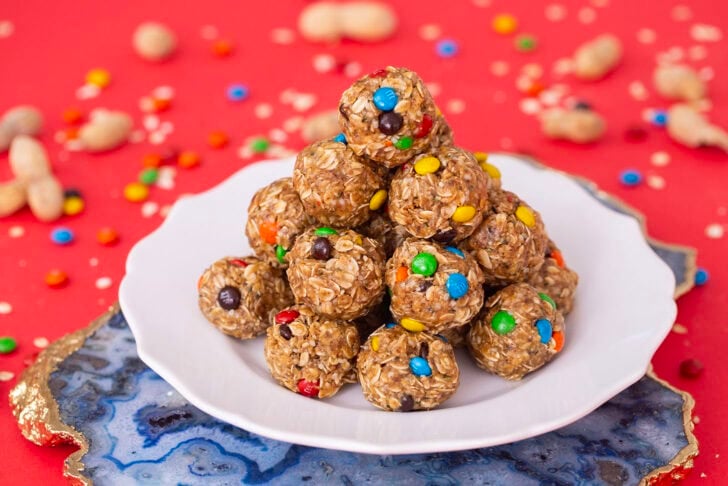 A pile of no-date protein balls on a white plate, sitting on a red table setting, as well as a blue marble cutting board.