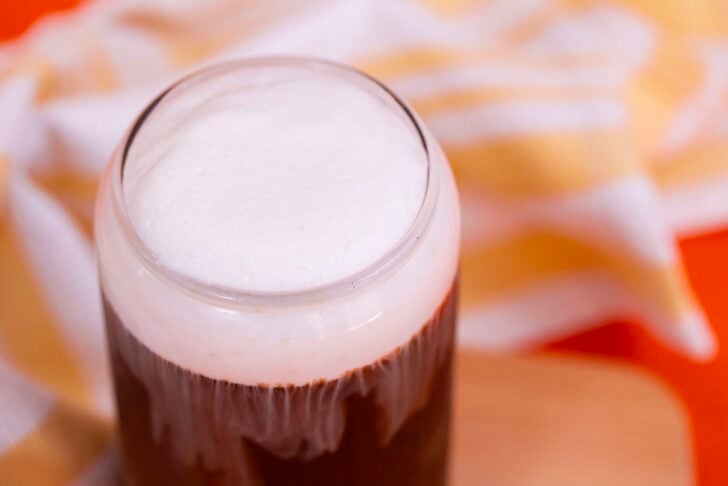 Iced coffee in a glass with vanilla sweet cream cold foam on a wooden cutting board.