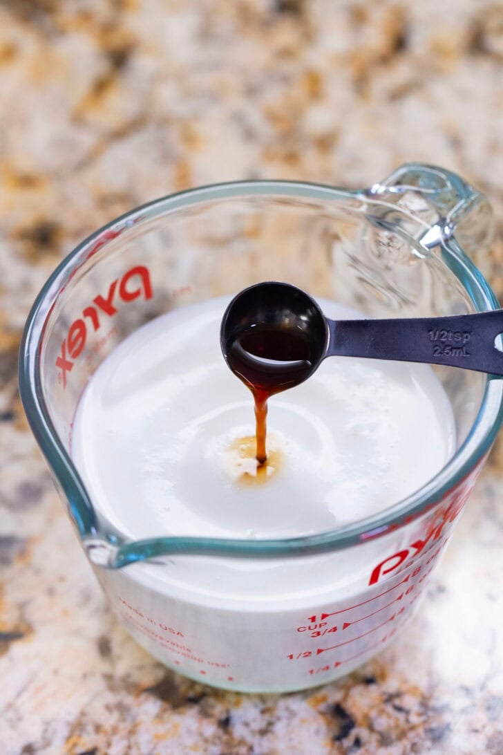 Pouring ingredients, specifically vanilla extract, into a measuring cup with the other ingredients for vanilla sweet cream cold foam. 