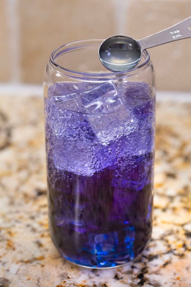 Adding lemon juice to the dirty soda mixture, the color changing from a cool blue to a vibrant purple.