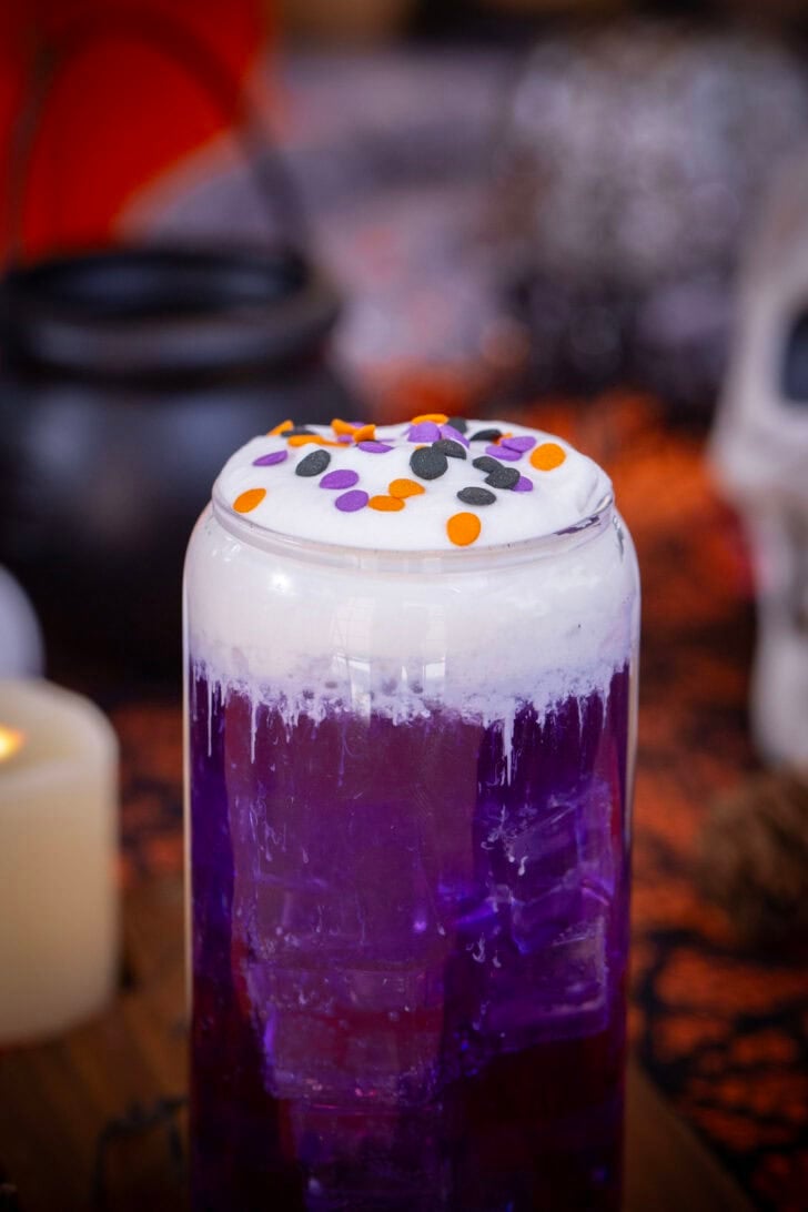 A close up shot of a purple halloween themed witch's brew dirty soda on a table with halloween decorations