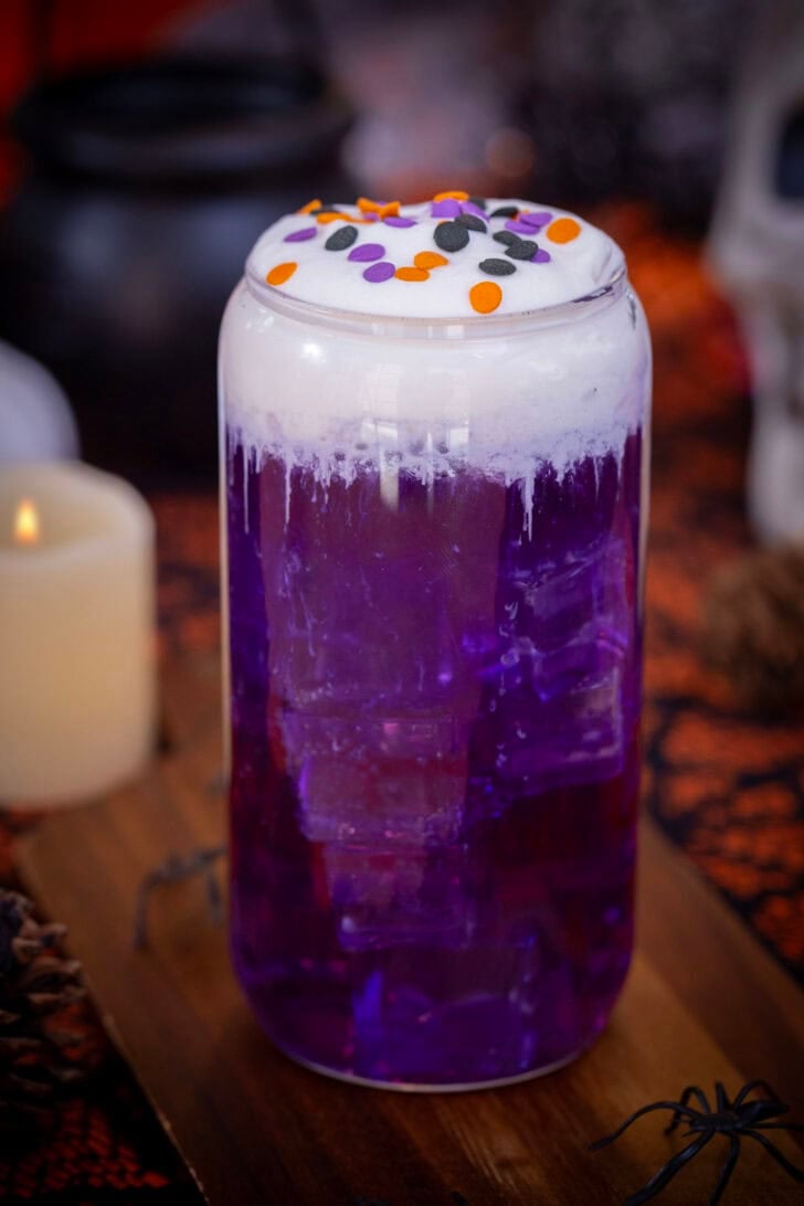 A purple, halloween themed witch's brew dirty soda on a table with halloween decorations