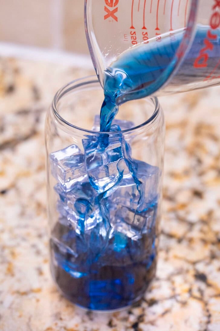 Pouring butterfly pea tea into a glass with ice.