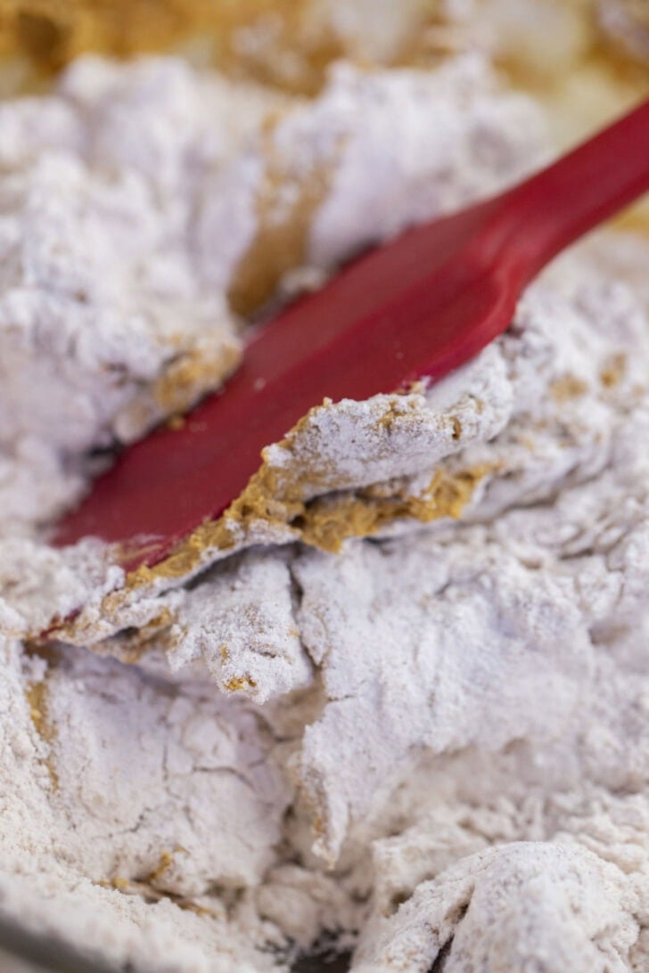 Folding flour into gingerbread cookie dough with a red silicone spatula.