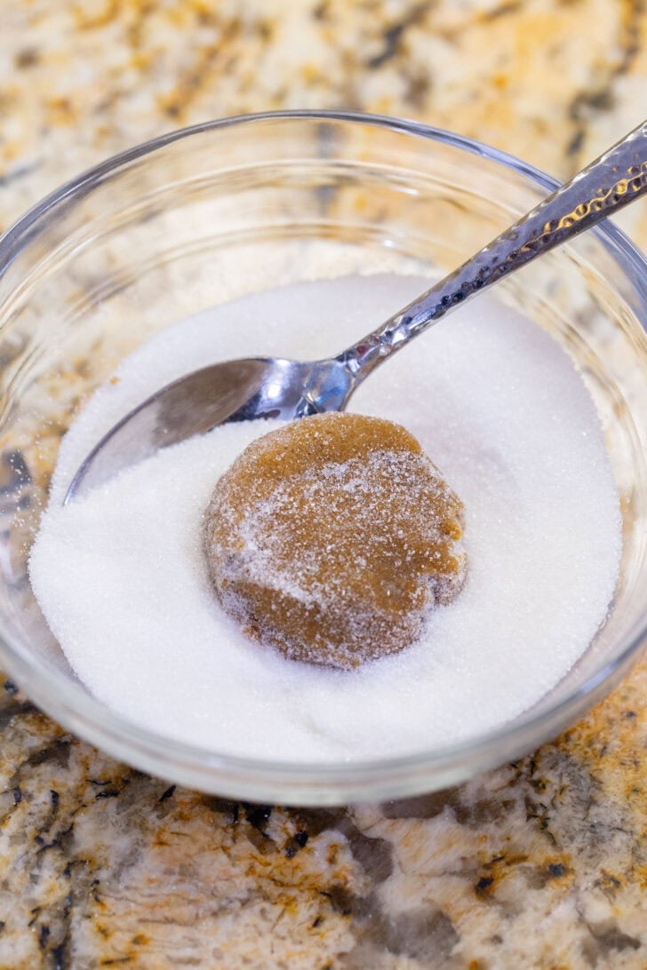 Rolling a ball of gingerbread cookie dough in granulated sugar.