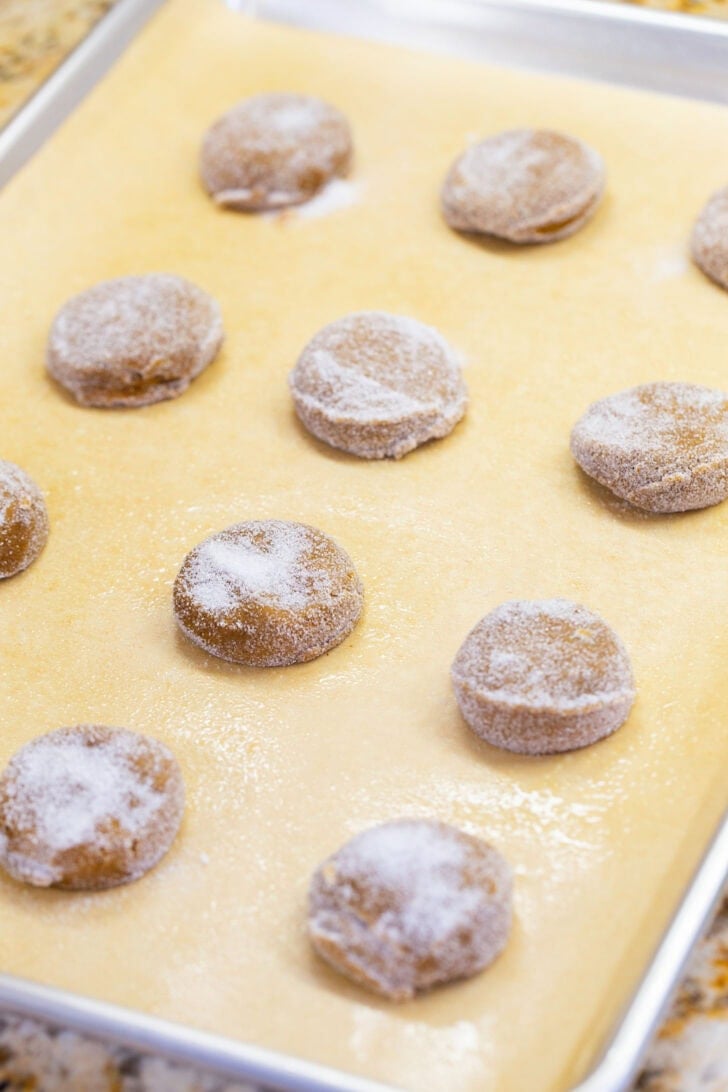 Sugar-coated eggless gingerbread cookie dough balls spaced apart on a parchment-lined baking sheet.