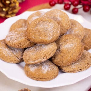 Soft gingerbread cookies with crackled sugar tops piled on a white scalloped plate on a festive red background.