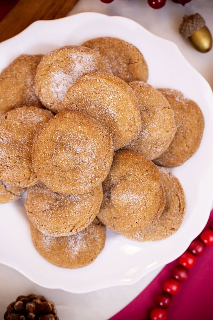 A high-angle shot of chewy gingerbread cookies piled on a white plate with holiday decorations around it.