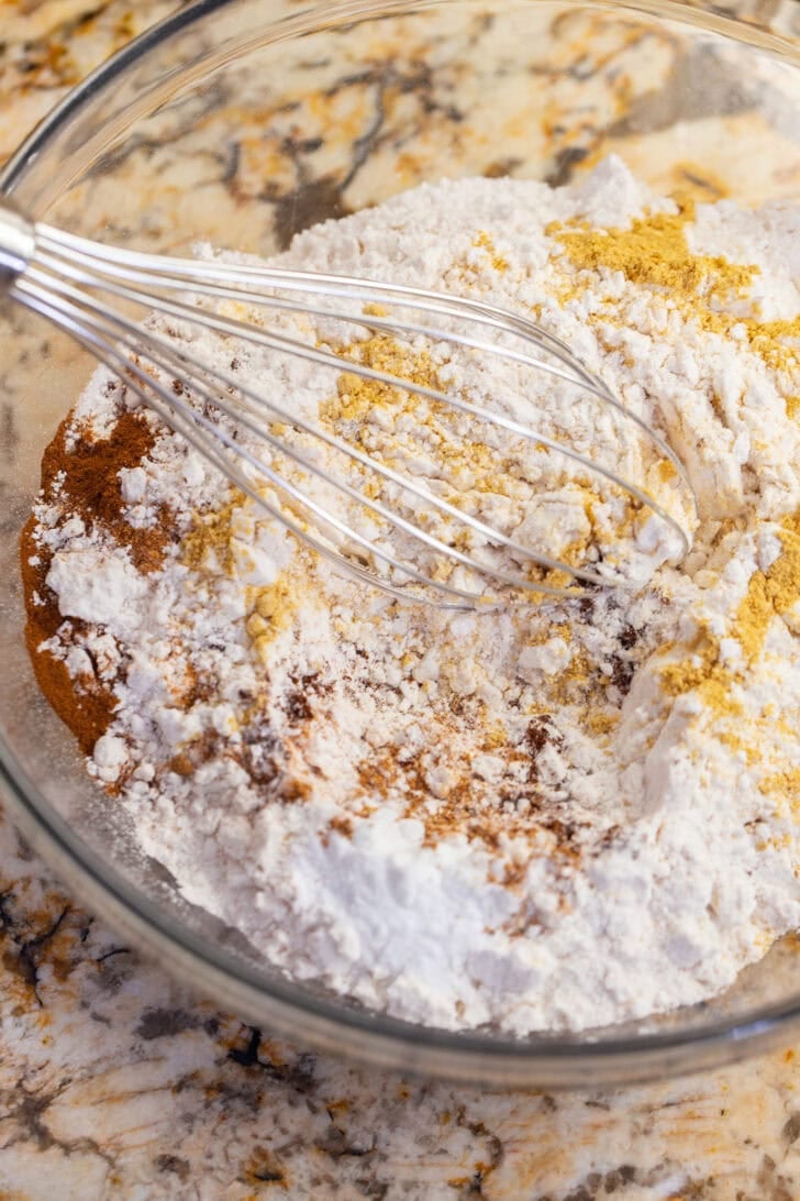 Whisking flour and gingerbread spices together in a glass mixing bowl.