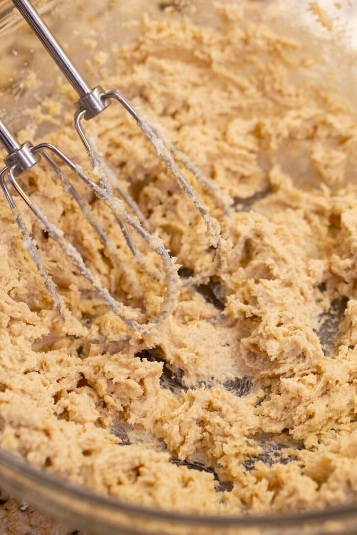Butter, brown sugar, and granulated sugar beaten smooth with a hand mixer in a glass bowl.