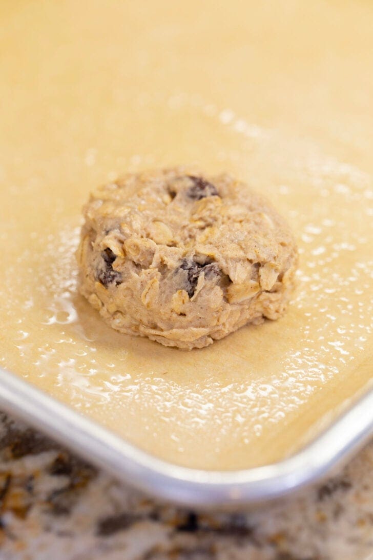 A flattened disc of eggless oatmeal raisin cookie dough on parchment paper, ready to bake.