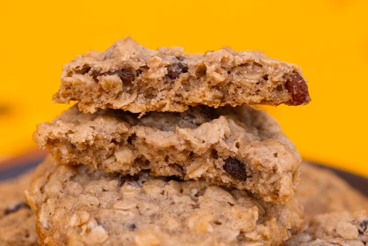 An eggless oatmeal raisin cookie broken in half to show its soft, chewy center with oats and raisins.