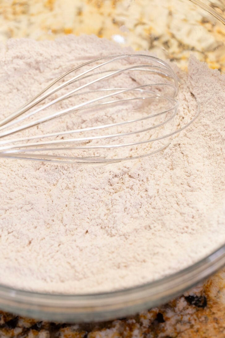 Flour, baking soda, salt, and cinnamon whisked together in a glass mixing bowl.