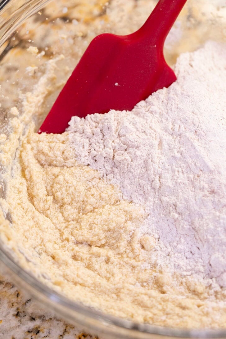 Adding the flour and cinnamon mixture to the creamed butter with a red silicone spatula.