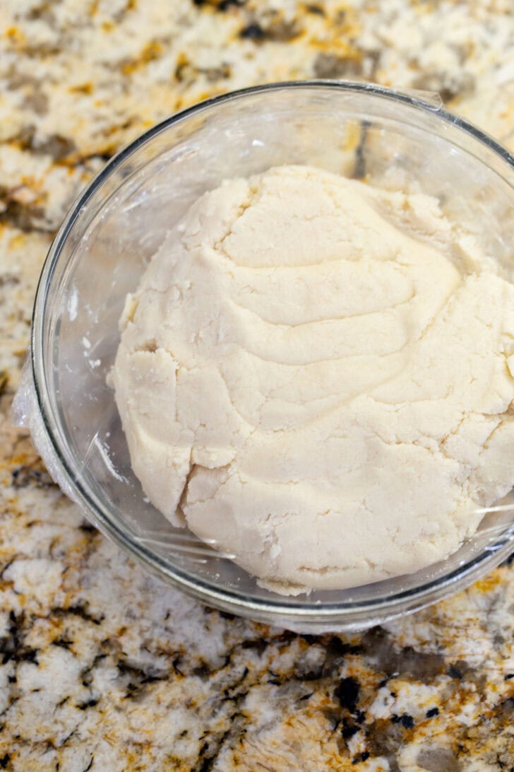 A ball of eggless snickerdoodle dough in a glass bowl, ready to chill in the fridge.