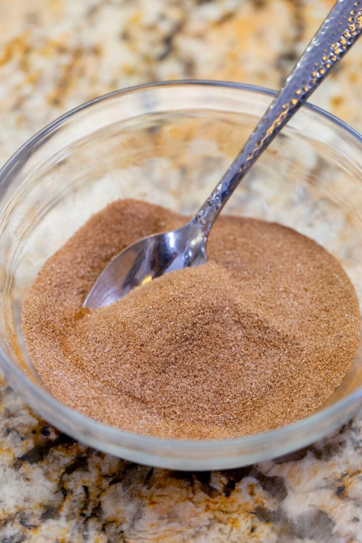 Cinnamon sugar stirred together with a spoon in a small glass bowl.