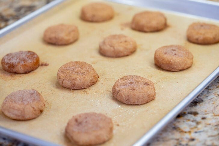 Cinnamon-sugar-coated eggless snickerdoodle dough discs spaced apart on a baking sheet, ready to bake.