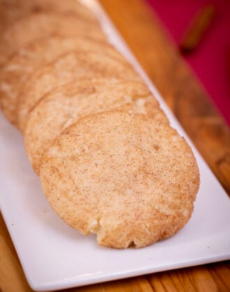 A close-up of soft, cinnamon-sugar-coated eggless snickerdoodles lined up on a white platter.