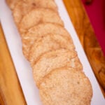 A long row of soft eggless snickerdoodles on a white platter set on a wooden board.