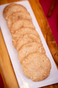 A long row of soft eggless snickerdoodles on a white platter set on a wooden board.