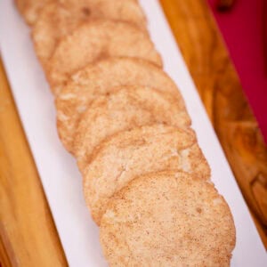 A long row of soft eggless snickerdoodles on a white platter set on a wooden board.