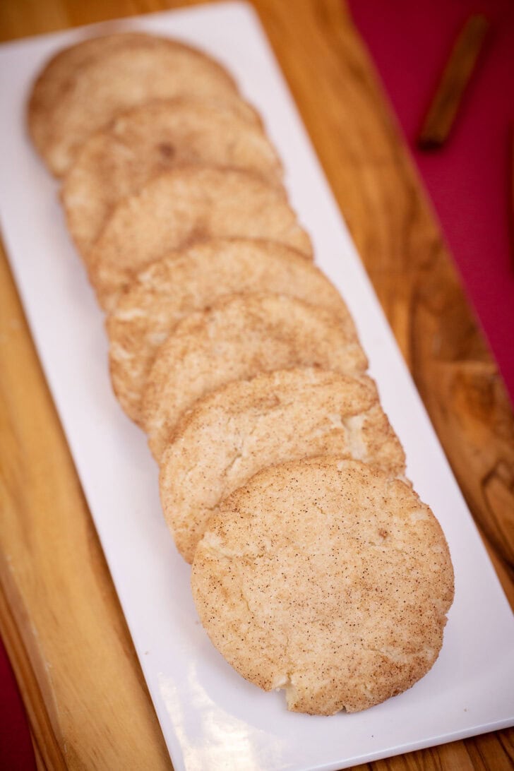 A long row of soft eggless snickerdoodles on a white platter set on a wooden board.