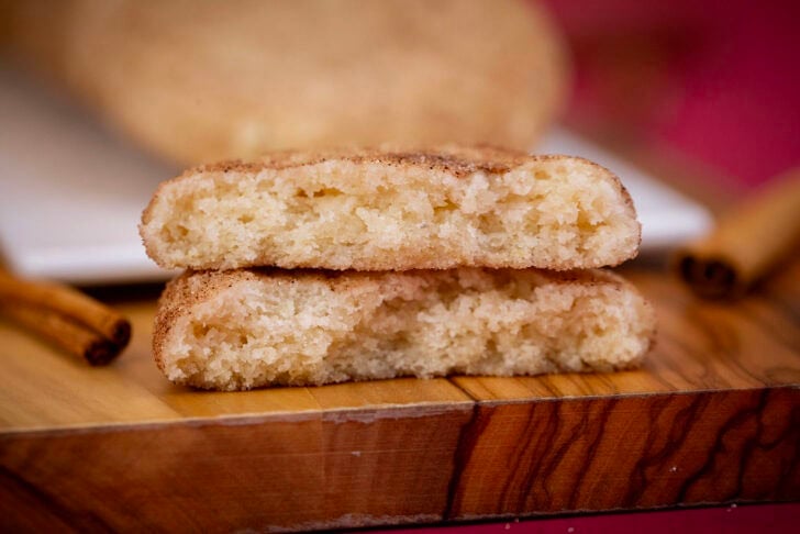 An eggless snickerdoodle broken in half and stacked to show its soft, chewy center, with cinnamon sticks nearby.