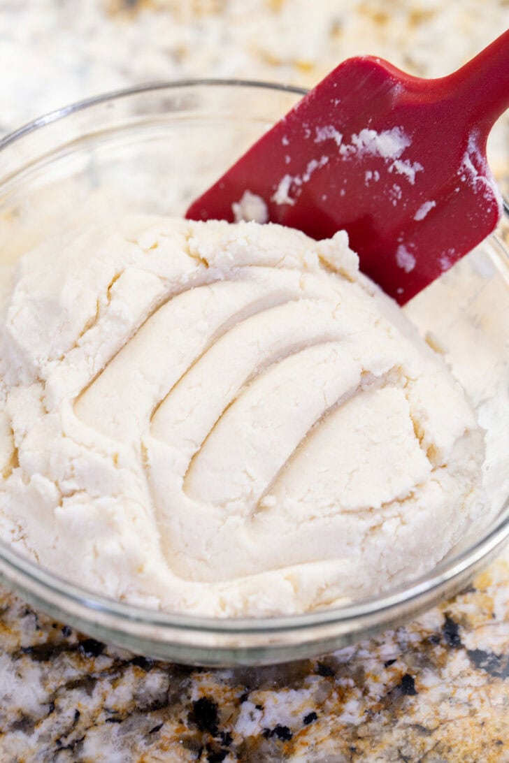 Soft eggless snickerdoodle dough mixed together with a red spatula in a glass bowl.