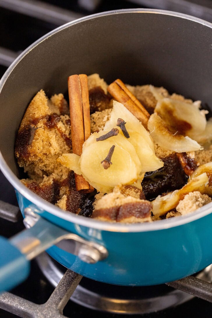Light brown sugar, molasses, sliced fresh ginger, cinnamon sticks, and whole cloves in a teal saucepan to make gingerbread simple syrup.
