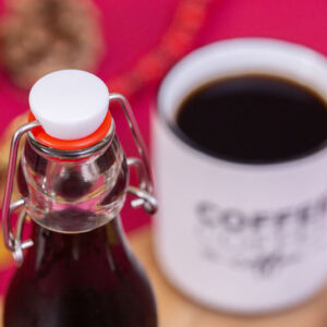 A high-angle shot of a glass bottle filled with gingerbread simple syrup next to a white coffee mug and gingerbread cookies.